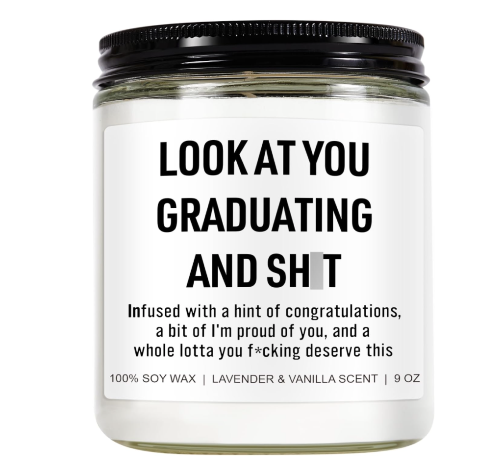 a candle with the label, "look at you graduating and sh*t." The letters are black. The background is white.