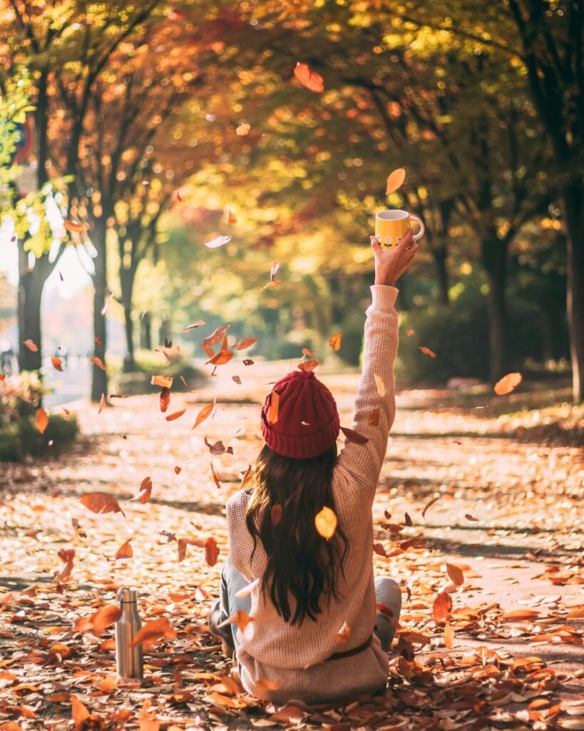 a baddie instagram caption worthy image of a woman sitting on the ground on a fall day. This is a back-facing pic not a forward-facing image. Gold fall leaves surround her