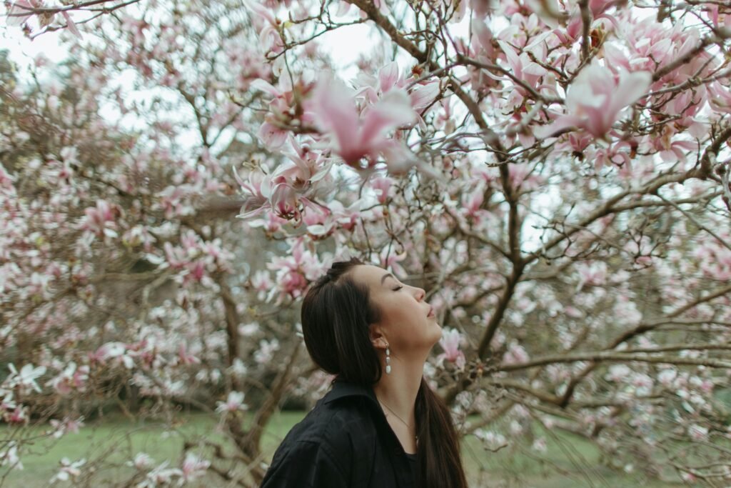 a woman is outdoors on a fall day taking in nature. Her face is aimed toward the sky with her eyes closed.