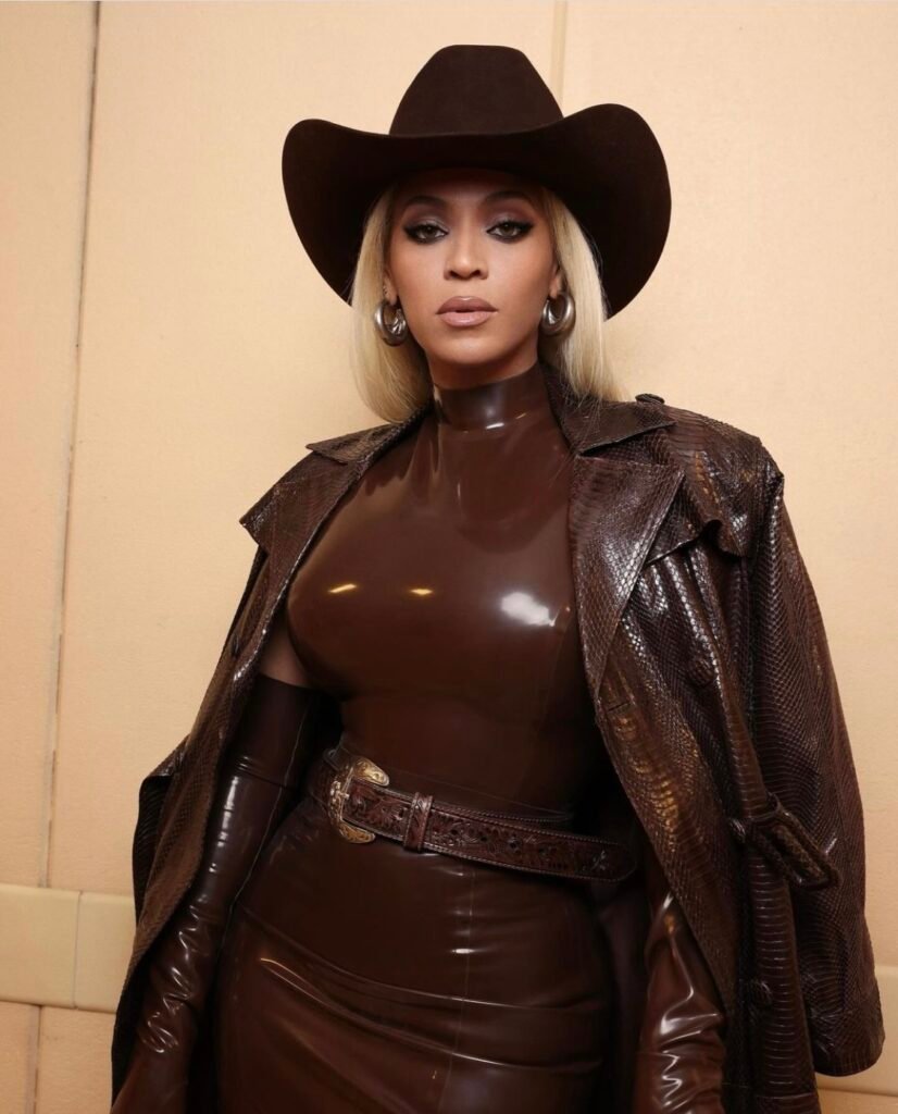 Beyonce (Cowboy Carter herself) decked out in beautiful brown leather and form-fitting dress with brown cowboy hat. The entire outfit is brown and expensive.