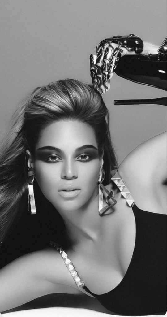 Beyonce Single Ladies. She is alone in this black and white picture, posing on the floor with 1 hand supporting her head and the other hand holding her high heel stilleto