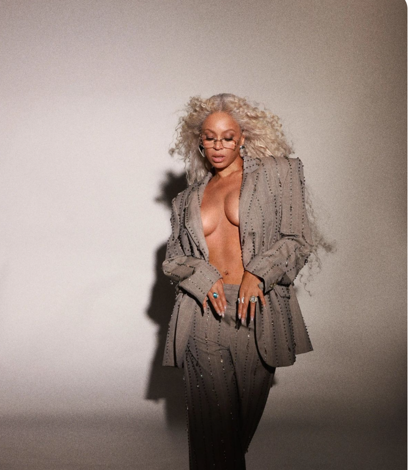 Beyonce with platinum blond hair, glasses, a pantsuit with a blazer with no shirt or blouse underneath blazer