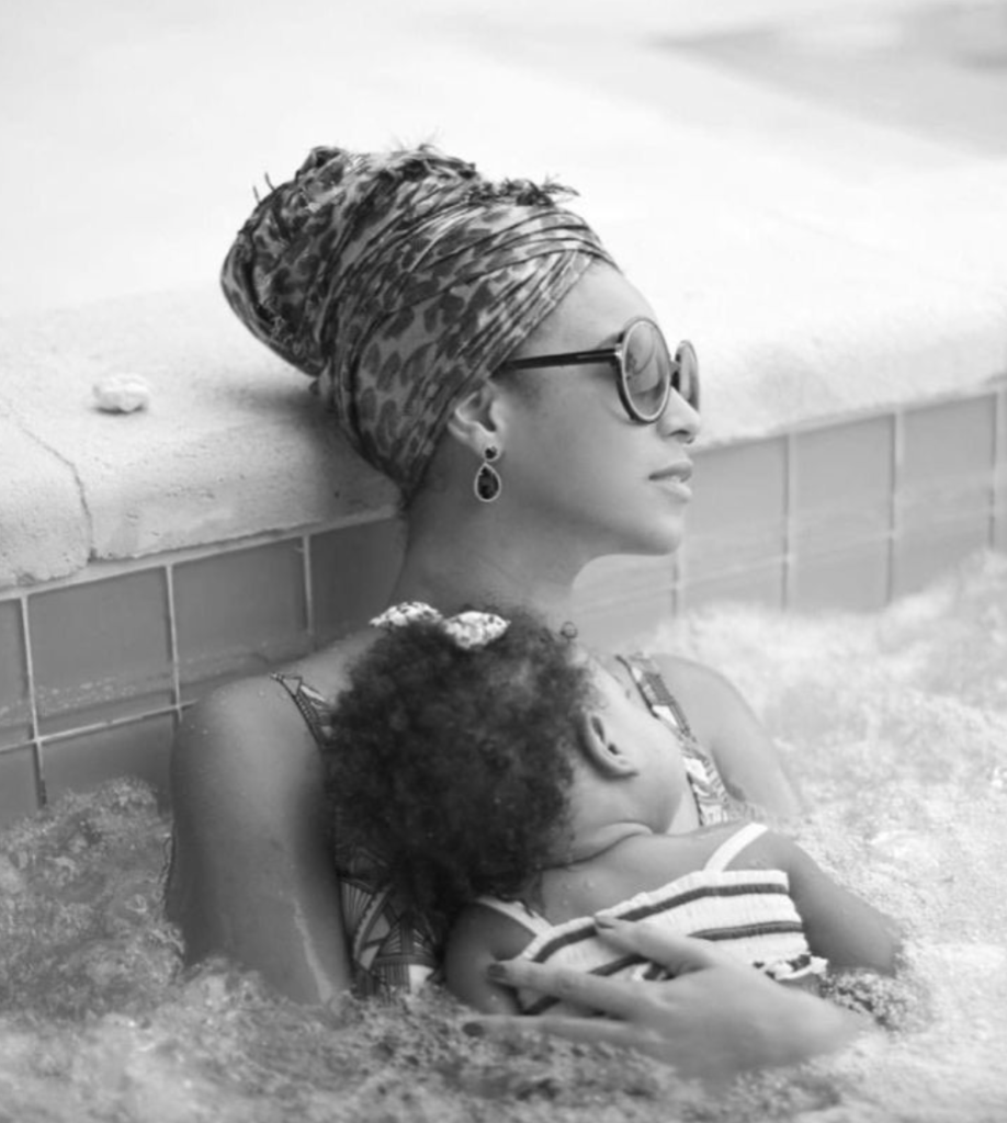 Beyonce and baby Blue Ivy Carter in the pool. The photo is in black and white. Beyonce is cradling Blue Ivy (who is a couple of months old) in her arms.