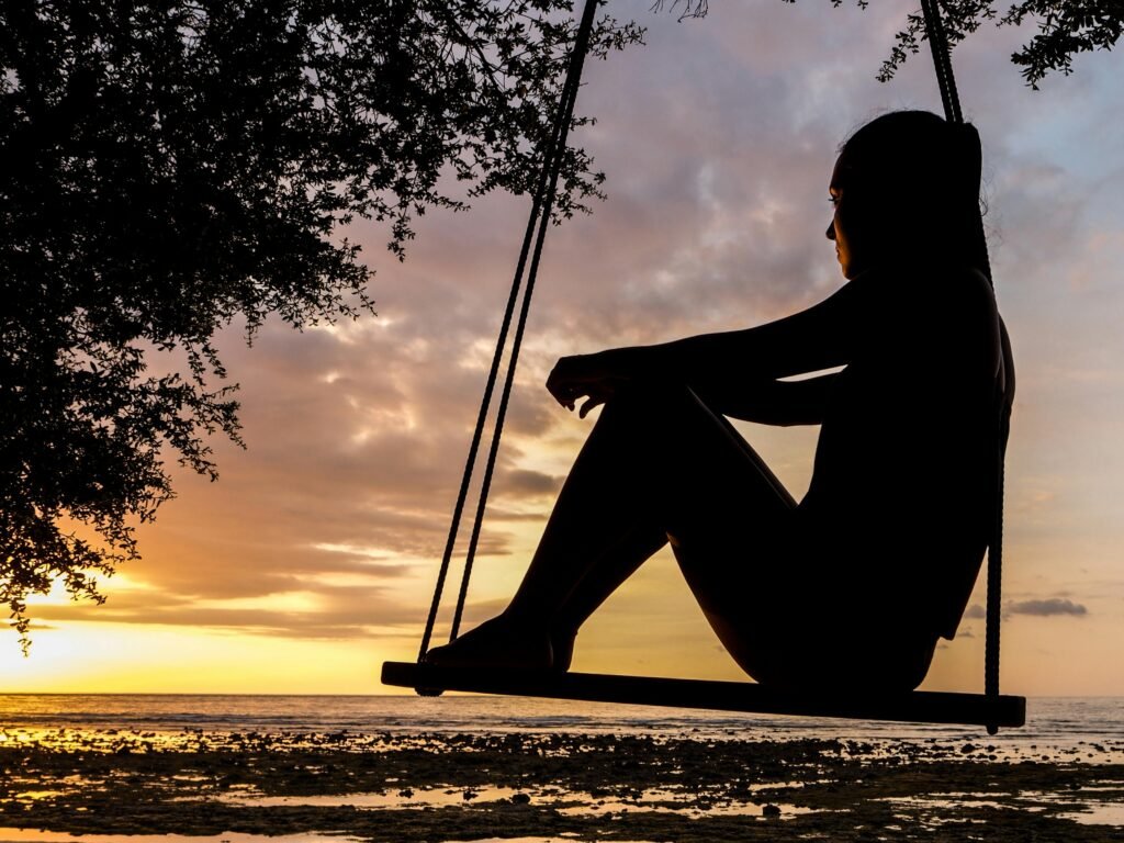 invest in yourself -a silhouette of a female figure peacefully sitting on a swing with a sunset background