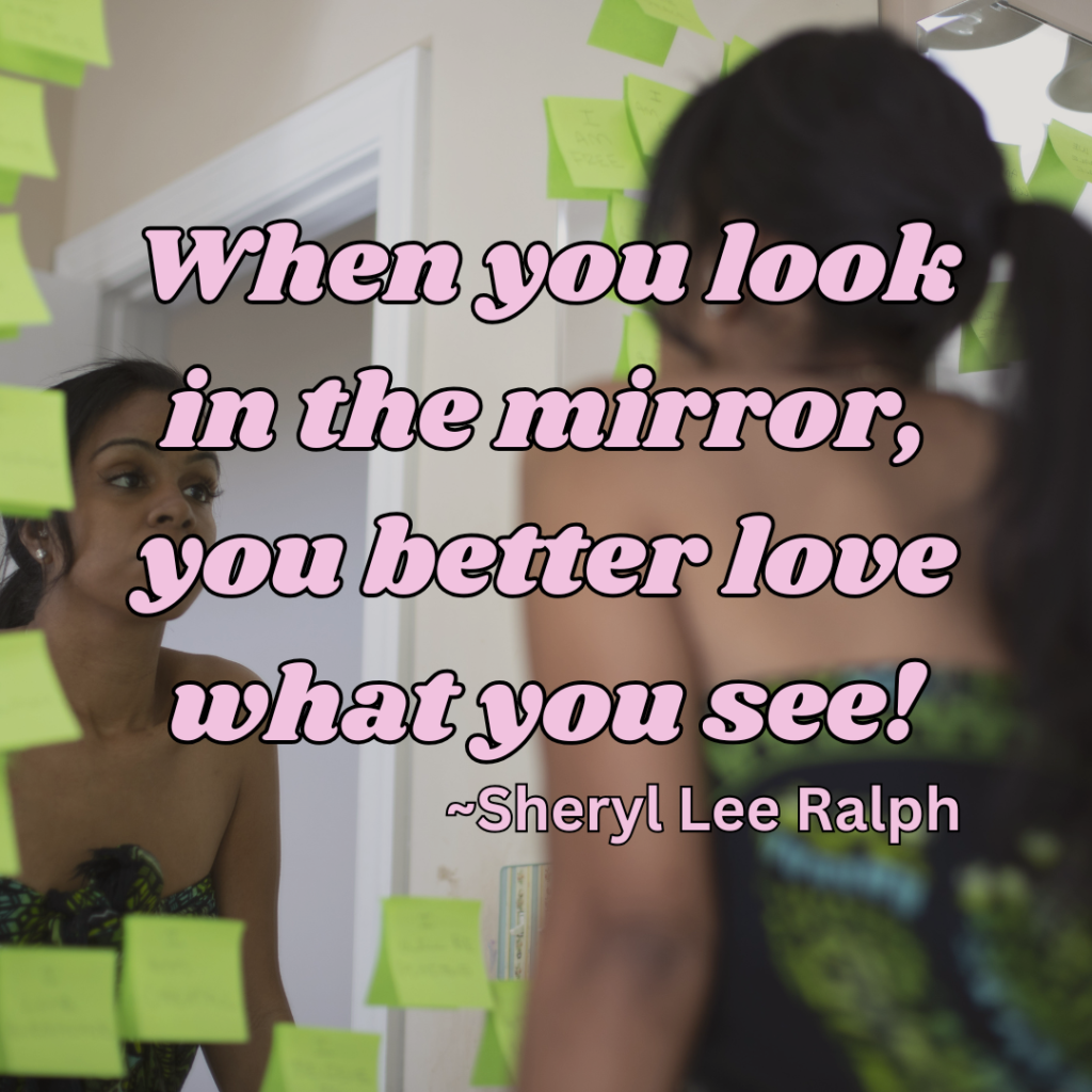 a young female is looking at herself in a mirror. The mirror has post-it notes on it in the shape of a heart