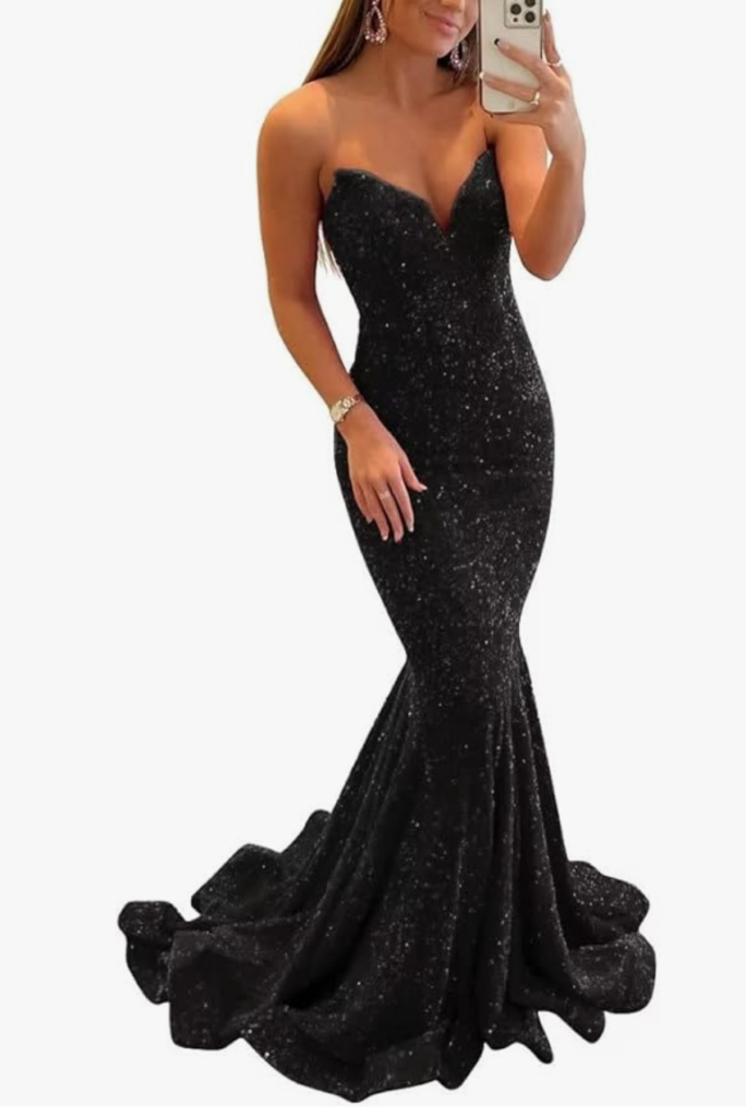 a woman models a strapless, form-fitting, full-length black evening gown/prom dress with sequins.At the base-from the ankle to the floor-is a flow of ruffles