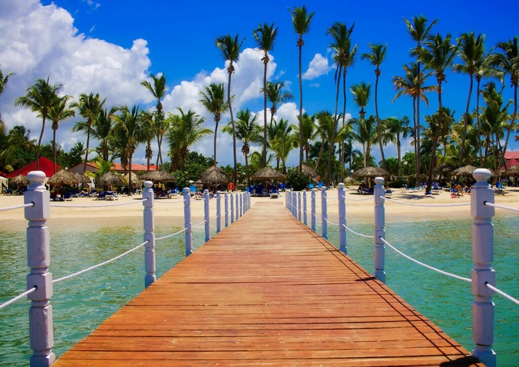 a sunny beach scene with crystal clear water, white sands, sunny blue skies, palm trees and a crossway (bridge) over the water