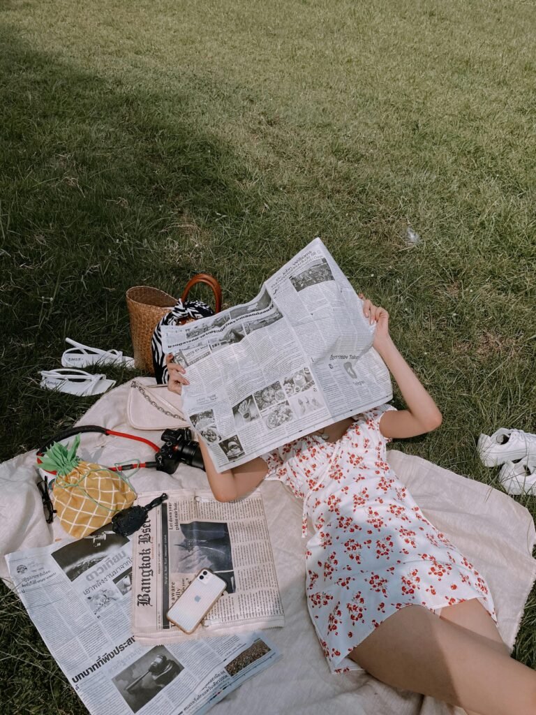 a college student relaxes during spring break on the grass with a blanket and newspaper
