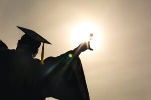 funny yearbook quotes: a silhouette of a graduate celebrating diploma up in sun