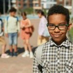 100 inspirational quotes for young black males like this young African American school boy wearing a backpack. He poses on the street with 4 other school children behind him.