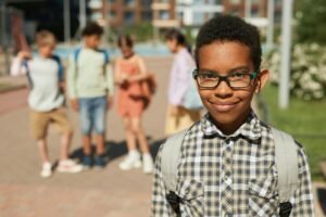 100 inspirational quotes for young black males like this young African American school boy wearing a backpack. He poses on the street with 4 other school children behind him.