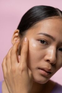 an Asian woman puts a dab of moisturizer on her "glass skin" face