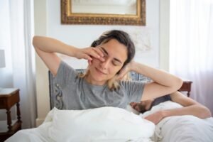 the featured image for this post - a woman waking and sitting up in her bed stretching with arms head level
