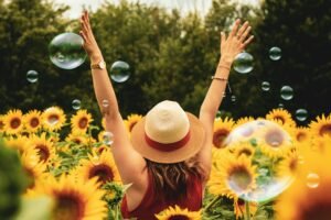 summer workout routine - a happy teacher is happy with arms outstretched toward the sky while standing in a sunflower garden and bubbles