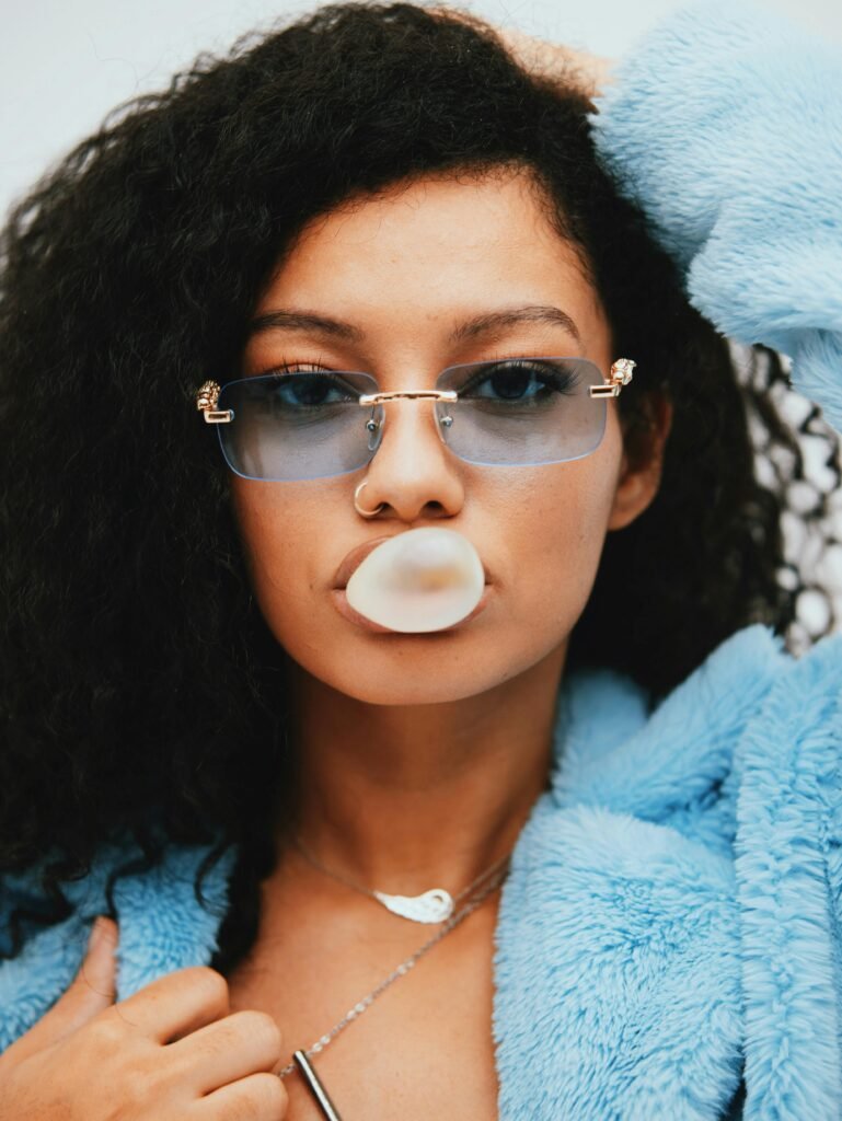 goddess energy hard usernames - a model wears a blue faux fur coat, blue shades, blowing a bubble with her bubble gum. Exudes attitude