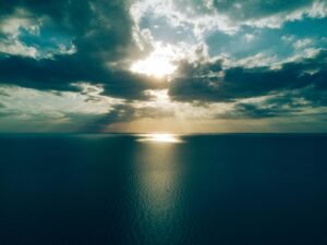 30 Day Blog Challenge - an image that represents serenity. An ocean, overall dark scene including the sky with a sliver of sun beaming off the ocean water