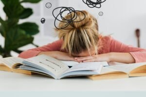 FEATURED IMAGE: get your life together - a woman lays her head down on her desk surrounded by clutter and open books in defeat