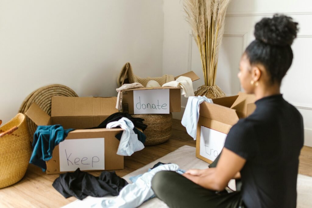 get your life together - a woman sits on her floor in front of 3 boxes labeled, "donate," "keep," "trash" decluttering her space