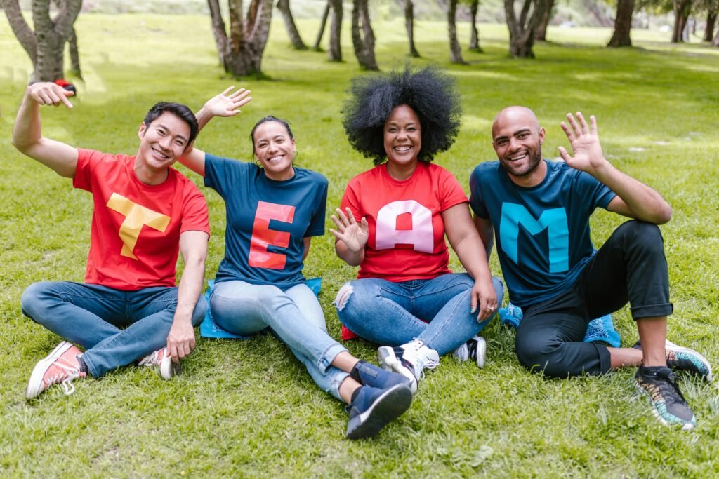 first day of school activities - a DIVERSE group of 4 sit outside on the ground with happy faces, jeans, and shirts that spell out the word, "TEAM"